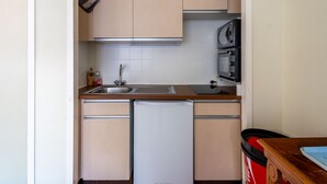 Una cocina compacta con un lavamanos, un microondas y un refrigerador pequeño.