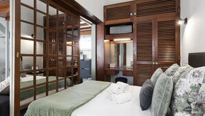 A hotel room with a bed, a green blanket, a wooden wardrobe, and a desk with a chair.