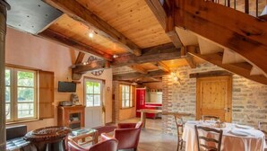 A rustic interior with a dining area, wooden beams, stone walls, and a staircase.