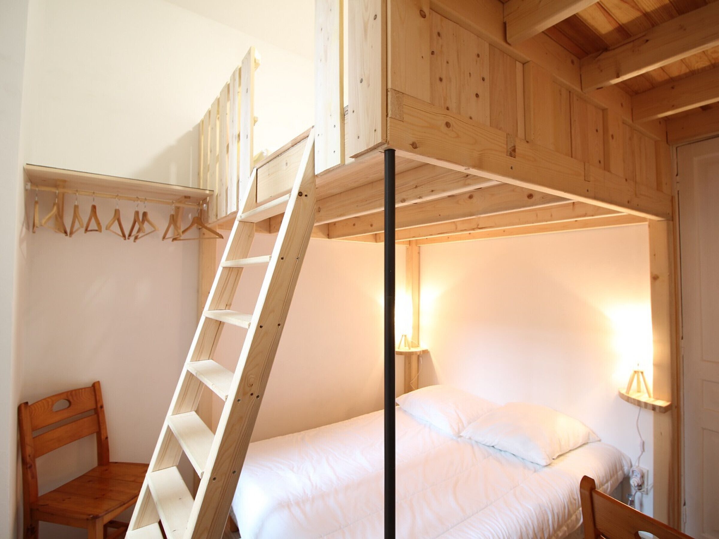 A bunk bed room with a wooden ladder, a chair, and a bedside lamp.