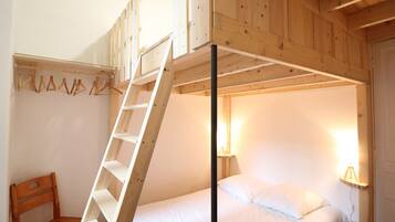A bunk bed room with a wooden ladder, a chair, and a bedside lamp.