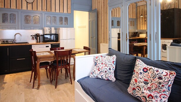 Un espacio habitable compacto con comedor, kitchenette y sofá con cojines estampados.