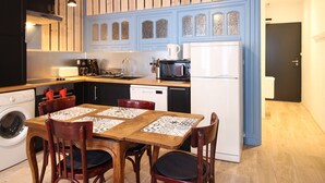 Una cocina compacta con armarios de madera, lavadora integrada, refrigerador blanco y una mesa de comedor con sillas.