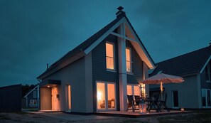 Une maison moderne dotée d’un grand patio, d’une table à manger et d’un éclairage extérieur.