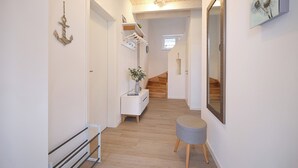 A hallway with wooden flooring, a white console table with a vase of flowers, a small grey ottoman, and a mirror on the wall. - Hyggehus - infrared sauna, terrace, fireplace, close to the beach and the North (Büsum)
