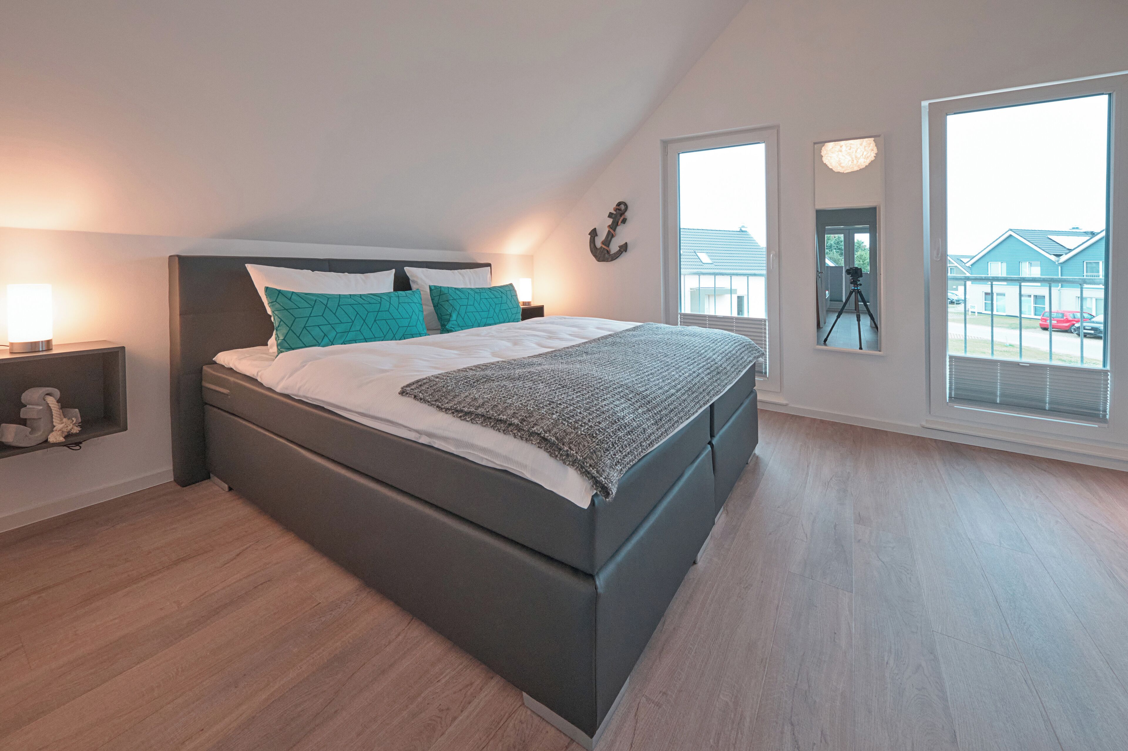 Une chambre moderne avec un grand lit, une table de chevet, une décoration murale en forme d’ancre et une vue sur l’extérieur par une fenêtre.