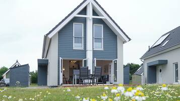 A two-story house with a gabled roof, a front porch with a table and chairs, and a garden with daisies.