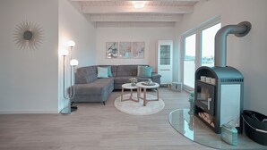 A modern living room with a gray sofa, round coffee tables, a fireplace, and large windows. - Hyggehus - infrared sauna, terrace, fireplace, close to the beach and the North (Büsum)
