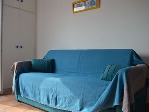 En blå sofa med et tæppe, en turkis pude og et billede i ramme på væggen.