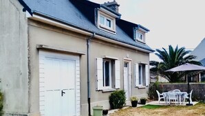 Ein zweigeschossiges Haus mit Garage, einer kleinen Terrasse mit Gartenmöbeln und einem gepflegten Rasen.
