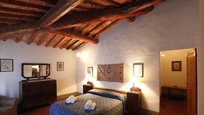Une chambre avec un plafond en bois, un lit avec des serviettes roulées, une commode et des œuvres d’art encadrées accrochées aux murs.