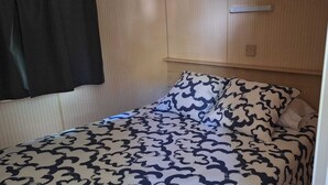 A single bed with a patterned bedspread and pillows, a wooden headboard, and a wall-mounted light switch. - Camping Rianxo (Rianxo)