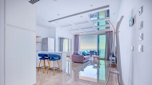 A modern hotel room with a kitchen, a living area with a sofa and chairs, and a balcony with a view of the sea. - Luxurious Apt With Ocean Views and Pool in Tigne Point (Sliema)