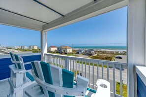 A balcony with white chairs and a view of the beach and ocean.