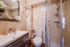 Ein modernes Badezimmer mit Duschkabine aus Glas, einem weißen Waschbecken mit zwei Handtuchhaltern und einer Toilette mit Pflegeprodukten.