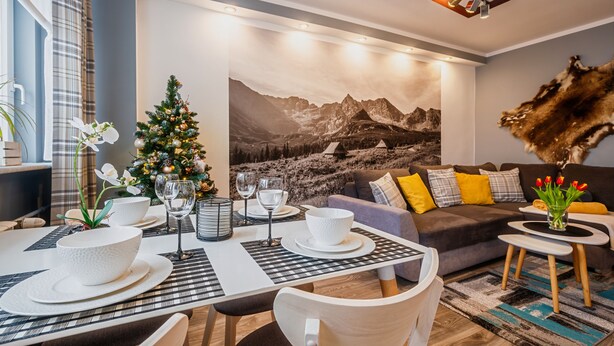 Un salon moderne avec un coin repas, agrémenté d’une fresque représentant un paysage de montagne, d’un sapin de Noël et d’un tapis en fourrure.