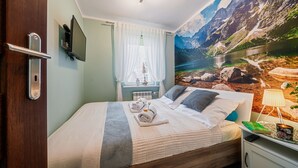 Une chambre à coucher comprenant un lit, une table de chevet, une lampe, un téléviseur et une fresque murale représentant un paysage de montagne.