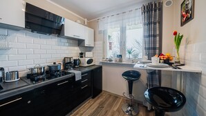 Une cuisine moderne avec des meubles blancs et noirs, un fourneau noir et une fenêtre donnant sur des arbres.
