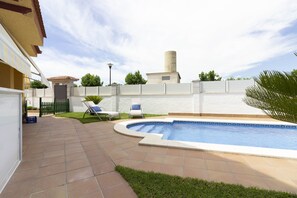 A swimming pool with a curved edge, a green lawn, and a white wall with a gate.
