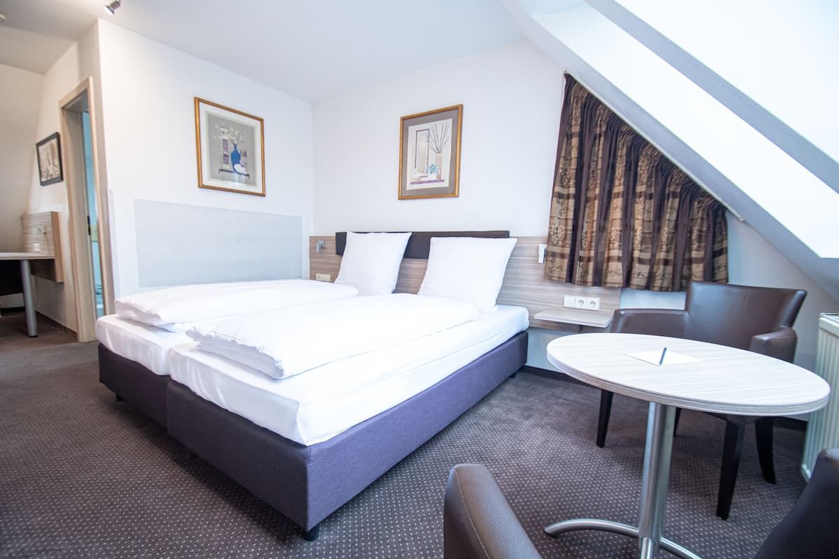 A hotel room with a large bed, a desk, a chair, and a small table.