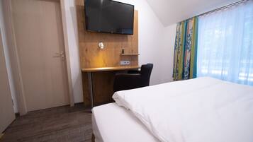 Ein Hotelzimmer mit einem Bett, einem Schreibtisch mit Stuhl, einem an der Wand montierten Fernseher und einem Fenster mit Vorhängen.