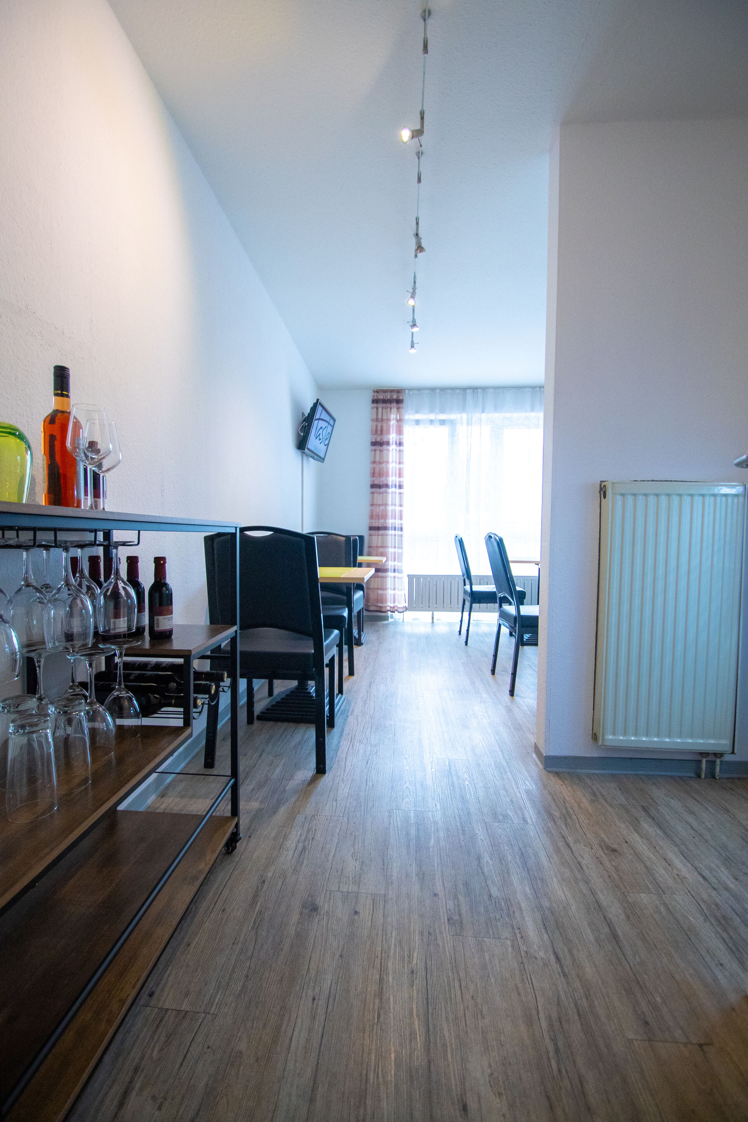 Un espace repas comprenant une longue table, des chaises et un meuble à vin où sont rangées des bouteilles et des verres.