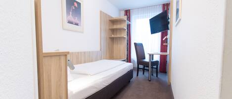 A compact hotel room with a single bed, a small desk, a chair, and a TV.