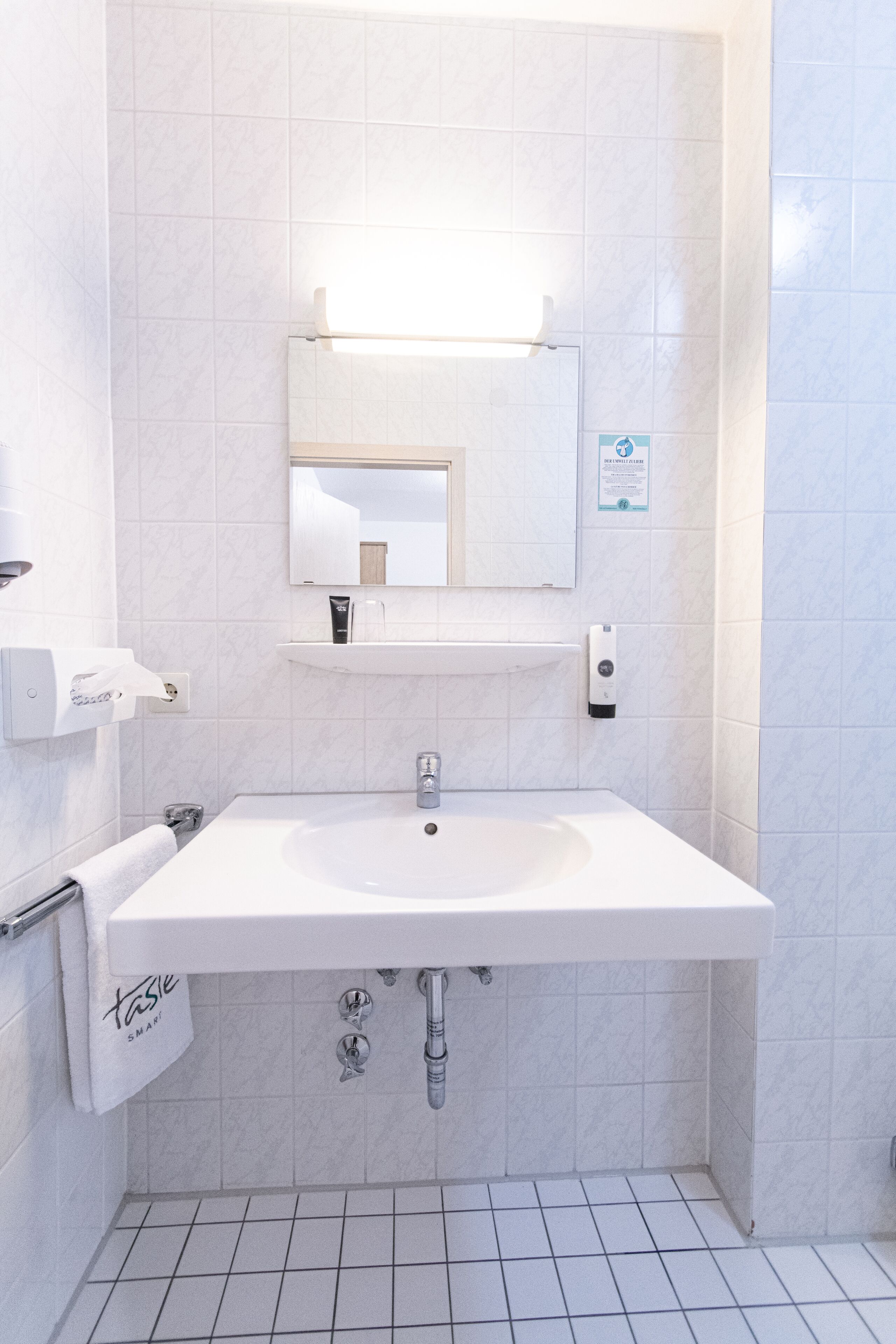 A modern bathroom with a white sink, mirror, and tiled walls.