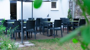 An outdoor seating area with multiple tables and chairs, a covered umbrella, and a stone wall in the background. - Taste Smart Hotel Backnang (Backnang)