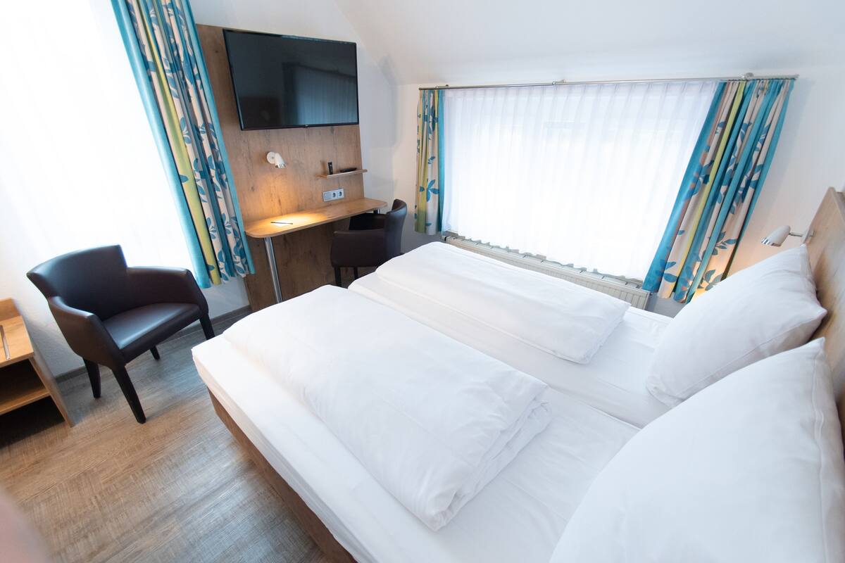 A hotel room with a large bed, a desk, a chair, and a TV mounted on the wall.