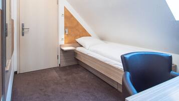 A small, modern room with a sloped ceiling, a single bed, a desk, and a chair.