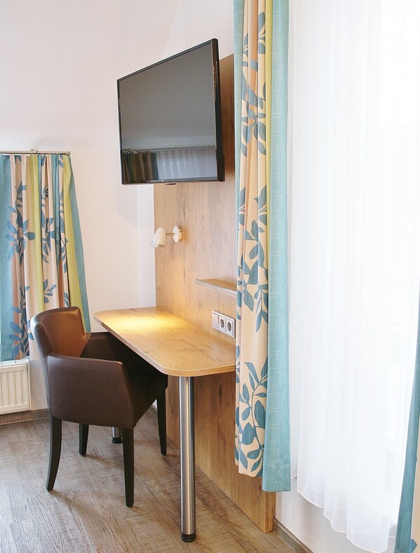 Una habitación compacta con escritorio de madera, dos sillones de cuero, un televisor montado y cortinas con estampado.