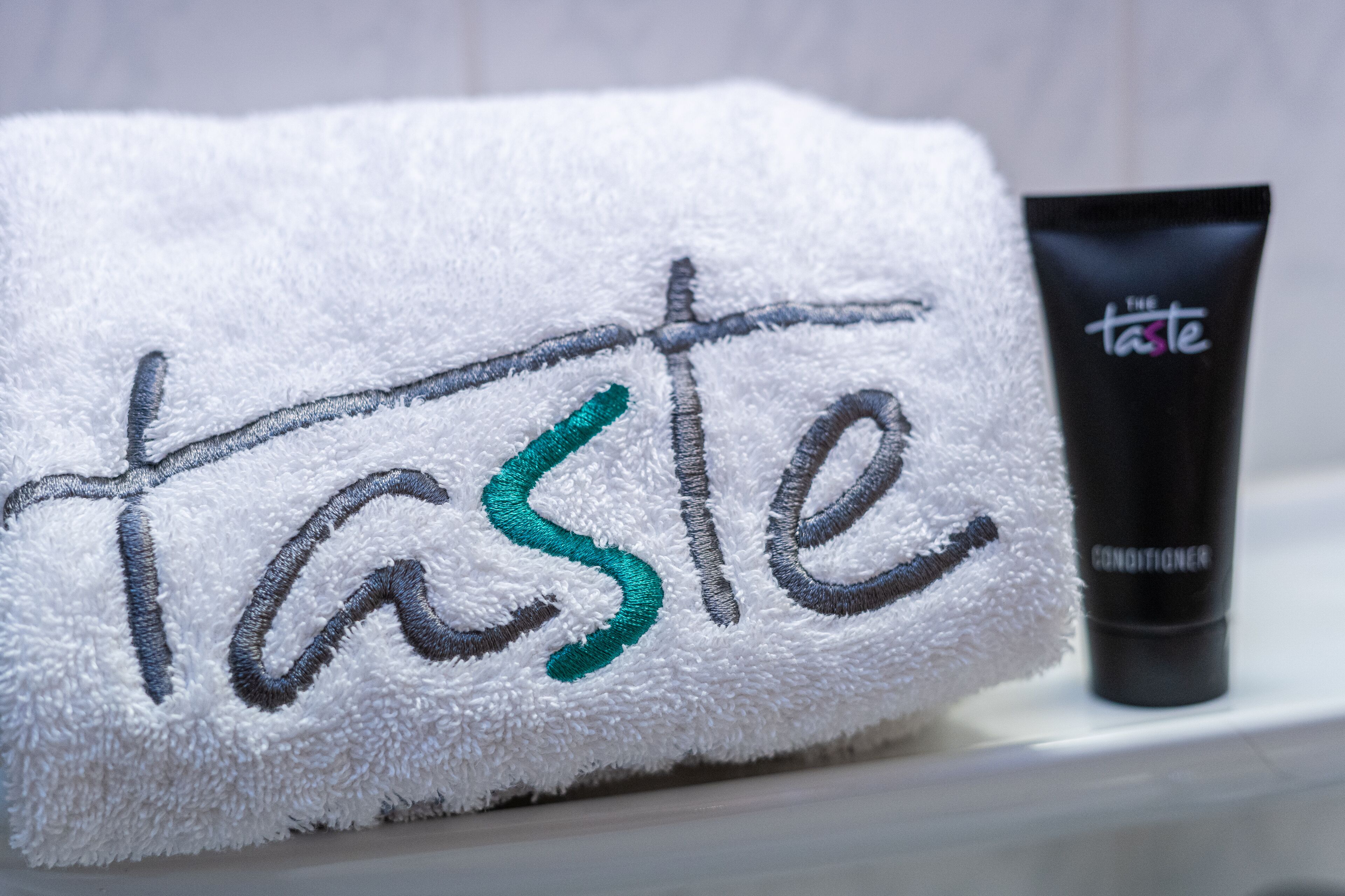 A white towel with embroidered text and a black tube of conditioner on a shelf.