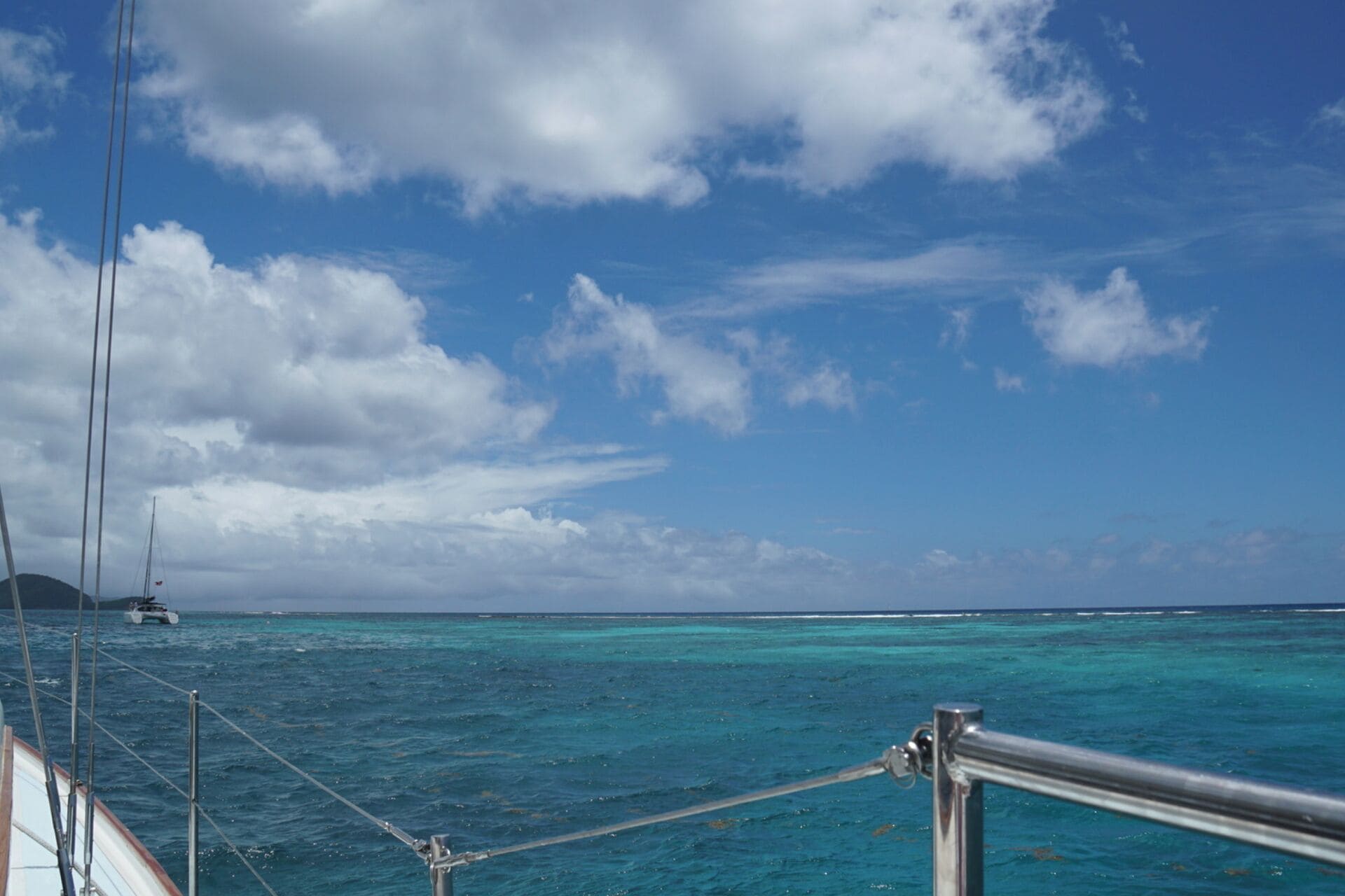 Un bateau doté d’une rambarde en métal, offrant une vue sur une eau turquoise et une île lointaine.