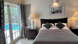 A bedroom with a bed, two bedside tables with lamps, a nightstand, a window with curtains, and a framed picture on the wall. - Villa - Sleeps 6 - Pool - Parking - Garden (Jolly Harbour)