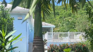 A small, single-story building with a blue exterior, a white porch, and a sign that reads "MOTHERHOOD". - Villa - Sleeps 6 - Pool - Parking - Garden (Jolly Harbour)