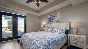 Un dormitorio con una cama grande, un ventilador de techo, obras de arte en la pared y vistas a través de la puerta.