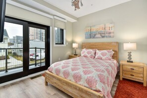 A bedroom with a large window, a bed with a patterned bedspread, two bedside tables with lamps, and a view of buildings outside. - Stunning 2 story luxury villa on 104th Street (Ocean City)