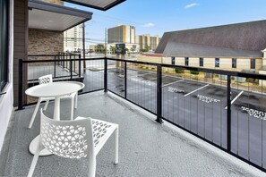 A balcony with a white table and chair, a view of a parking lot, and buildings in the background. - Stunning 2 story luxury villa on 104th Street (Ocean City)