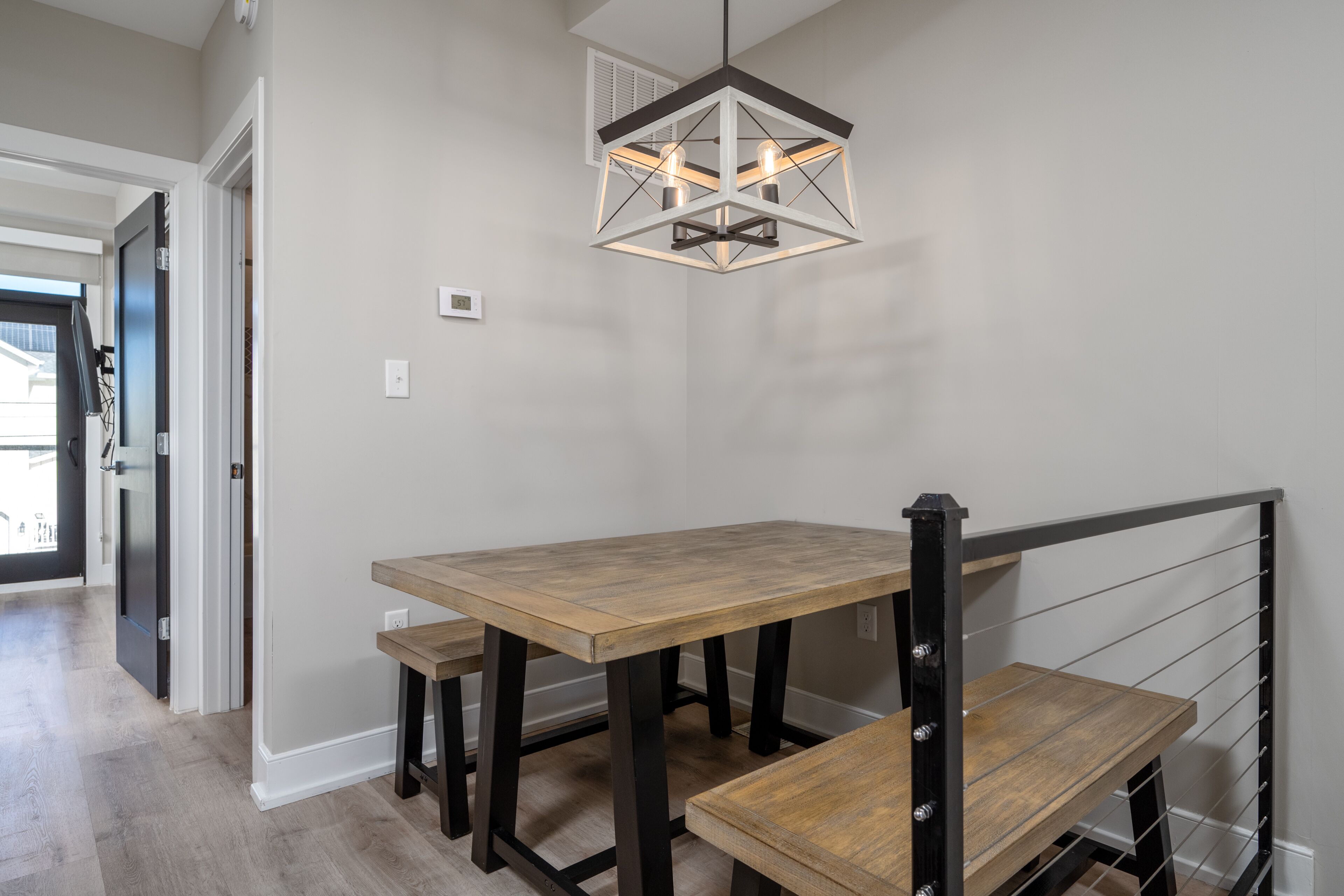 A dining area with a wooden table and bench, a hanging light fixture, and a staircase with a metal railing.