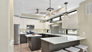 Una cocina moderna con una isla grande, armarios oscuros y un salpicadero de azulejos pequeños.