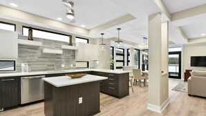 Una cocina moderna con una isla central, armarios oscuros y un ventanal grande.