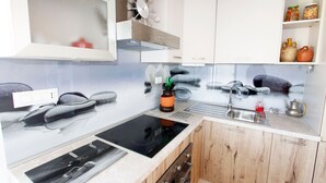Eine Küche mit weißen Schränken, einer schwarzen Induktionskochplatte, einer Edelstahl-Spüle und Holzschränken.