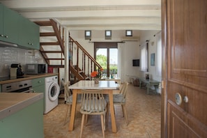 Una cocina con lavadora, sillas de madera, una mesa de comedor y una escalera.