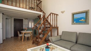 A living room with a sofa, a glass coffee table, a dining table with chairs, a staircase, and a painting on the wall. - Stylish sea view studio Artemis, Rhodes-Ialysos (Ialisos)