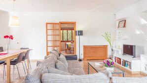 Una sala de estar con sofá, mesa de centro, televisor, estantería y un comedor con sillas y mesa.