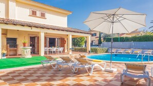 Un área junto a la piscina con sillones, una sombrilla grande y un suelo a cuadros.