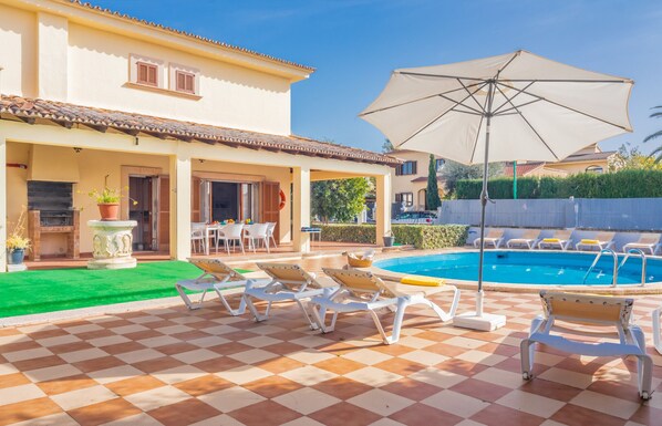 Un espace aménagé au bord de la piscine, avec des chaises longues, un grand parasol et un sol à carreaux.