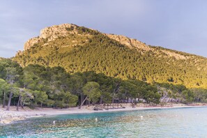 Une plage à l’eau turquoise et limpide, une colline rocheuse couverte d’une végétation luxuriante, et une rive sablonneuse parsemée de quelques constructions.