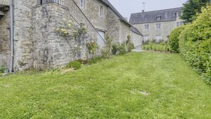 A stone building with a staircase leading to a second floor, surrounded by a well-maintained lawn and a hedge.
